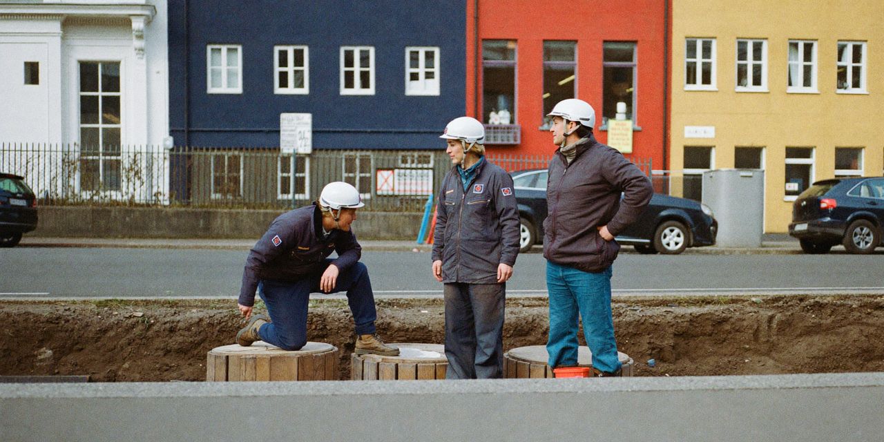Cable jointers in helmets at an opened street trench with cable drums on a Stockholm street