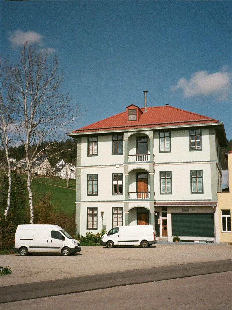 Renovated guesthouse with a red roof and two white vans in the yard