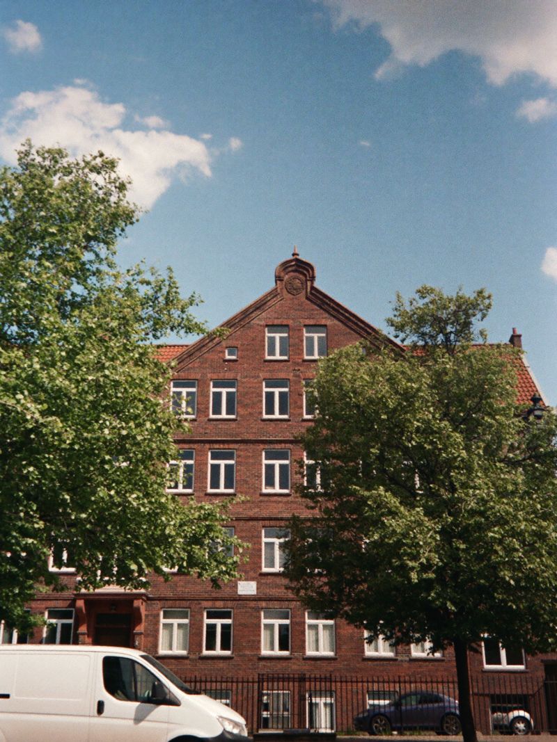 Red-brick apartment building on a tree-lined street with a white van in front